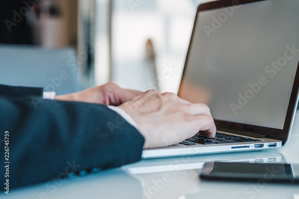 Fototapeta Businessman's hands using laptop for work and mobile phone at office. Concept of using modern devices for work and maintaining communication. 