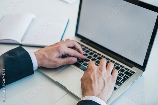 Fototapeta Businessman in black suit and white shirt using laptop for work at office. Concept of using technology for work. Horizontal.