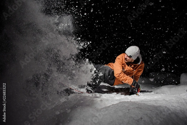 Fototapeta Snowboardzista w pomarańczowej kurtce jadący nocą na zaśnieżonym wzgórzu