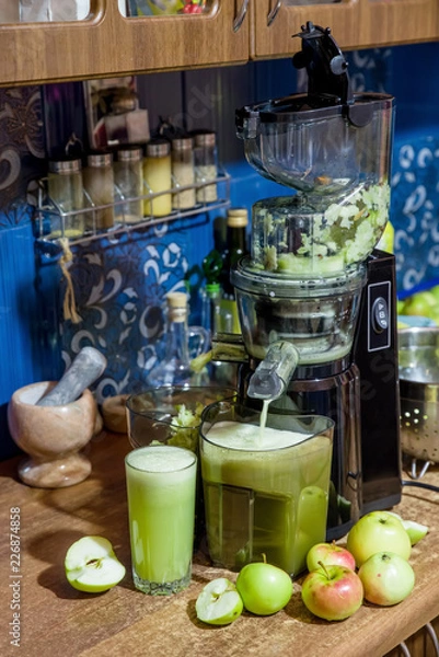 Fototapeta apple juice flowing from the juicer on the table in the kitchen