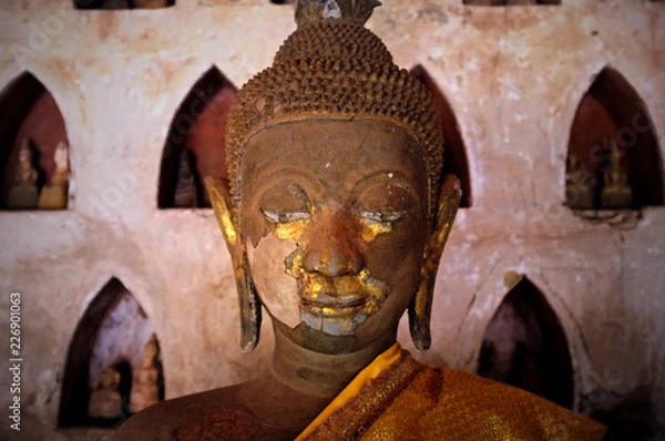Fototapeta gold plated theravada buddhist statues at a monastery with a orange silk cloth