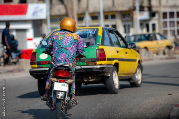 Obraz Motocykl w ruchu Cotonou, Benin. Mieszkańcy Beninu w życiu codziennym, styl życia Afryki Zachodniej. Moda z Beninu w Afryce Zachodniej.