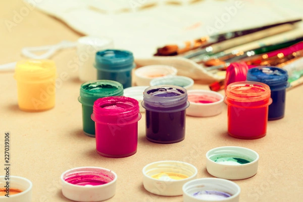 Fototapeta Jars with colorful gouache and brush on beige background close up
