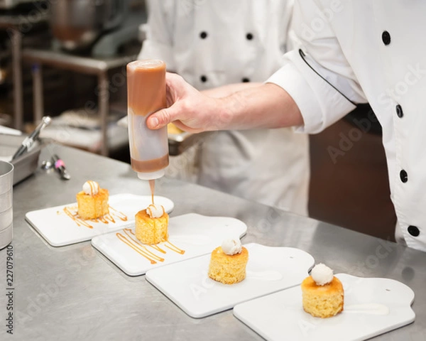 Obraz Man in a kitchen drizzling caramel sauce on small cakes topped with cream.