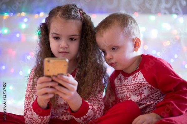 Obraz children in Christmas pajamas playing smartphone