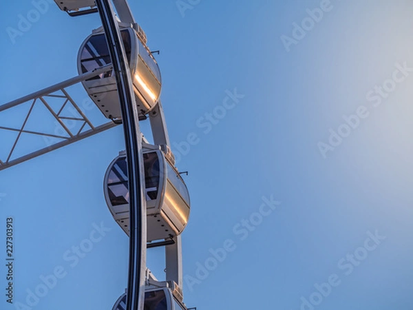 Fototapeta Low angle shot to a part of big wheel in playground park. Worm eye view Image of Ferris wheel. Uprise to look at a part of machine in sunny day. Take angle elevation to a beautiful blue sky.