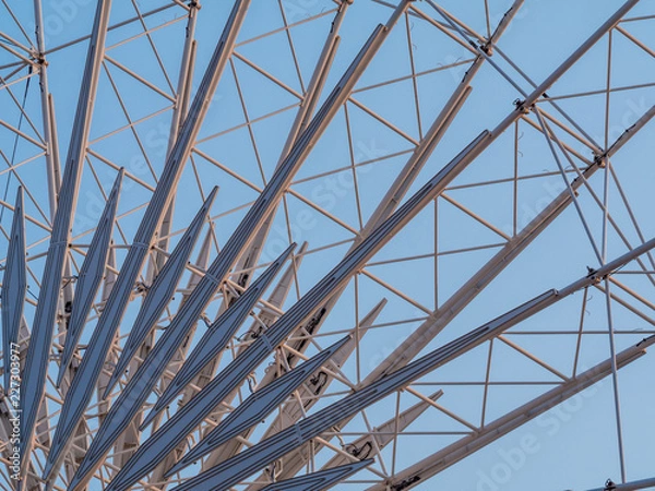 Fototapeta Low angle shot to a part of big wheel in playground park. Worm eye view Image of Ferris wheel. Uprise to look at a part of machine in sunny day. Take angle elevation to a beautiful blue sky.