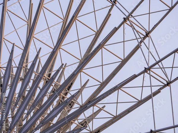 Fototapeta Low angle shot to a part of big wheel in playground park. Worm eye view Image of Ferris wheel. Uprise to look at a part of machine in sunny day. Take angle elevation to a beautiful blue sky.