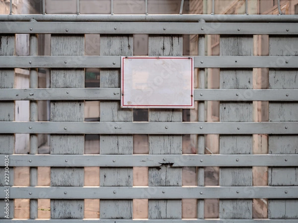 Fototapeta Blank white board hang on entrance gate. Empty text on attention board. Old vintage wooden fence with no people at abandoned house.