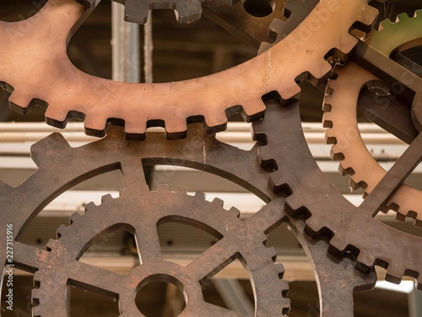 Fototapeta Low angle view to part of cogwheels. Vintage iron machine part in store. Abstract background of old industrial.