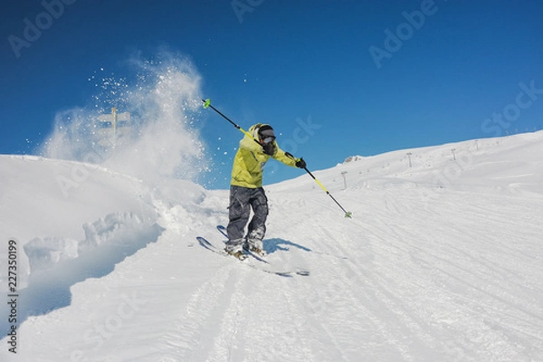 Fototapeta Aktywny narciarz w jasnożółtej odzieży sportowej jadący w dół po górach