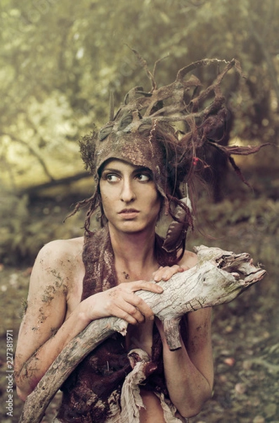 Fototapeta woman in a suit of felt and make-up of natural remedies and forest debris, the Dryad hides in an old garden under the trees