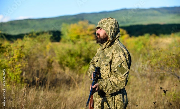 Fototapeta Okres polowań. Brodaty myśliwy mężczyzna z karabinem na tle przyrody. Doświadczenie i praktyka sprzyjają polowaniu na sukces. Jak zmienić polowanie w hobby. Facet polujący na przyrodę. Męskie hobby