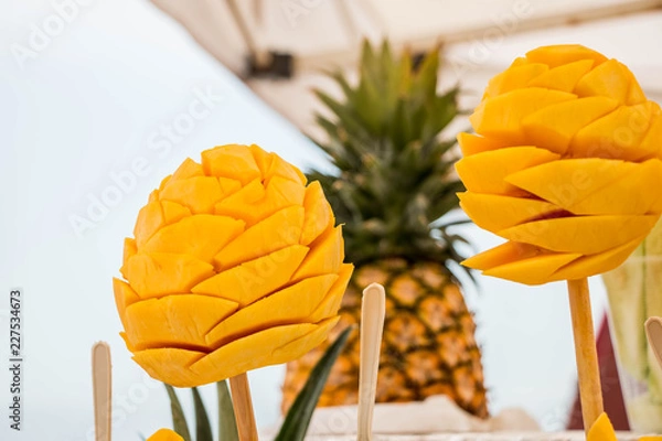 Fototapeta Mangos en palito, bocadillo típic Mexicano, con una piña en segundo plano al fondo.