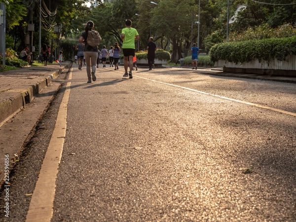 Fototapeta Selective focused on foreground at pathway with emotion blurred background. Rear view of people who are walking and running in public park. Low selection view of the way forward.