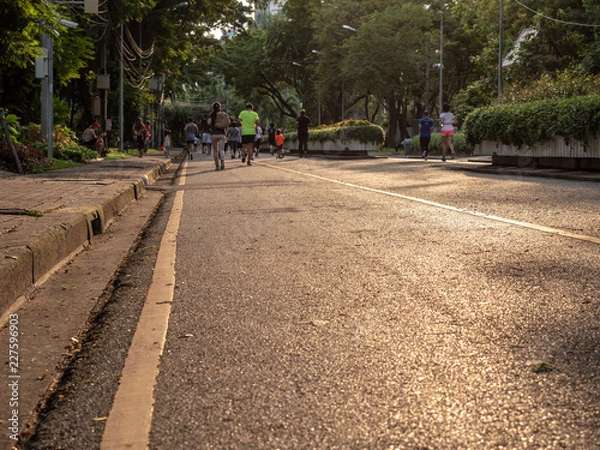 Fototapeta Selective focused on foreground at pathway with emotion blurred background. Rear view of people who are walking and running in public park. Low selection view of the way forward.