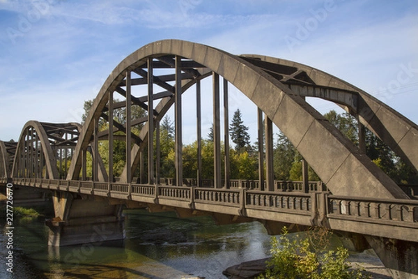Fototapeta Angular side view of precast concrete vehicle bridge with river flowing beneath and blue sky and wispy white clouds above