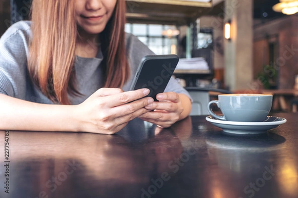 Fototapeta Closeup image of a woman holding and using a smart phone with coffee cup on table
