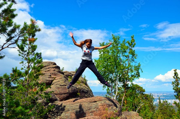 Fototapeta Girl jumping from a high cliff. The status of the flight. Beautiful autumn forest. Autumn in the mountains. Unity with nature. Beautiful view from the top. Mountaineering. Tourism.