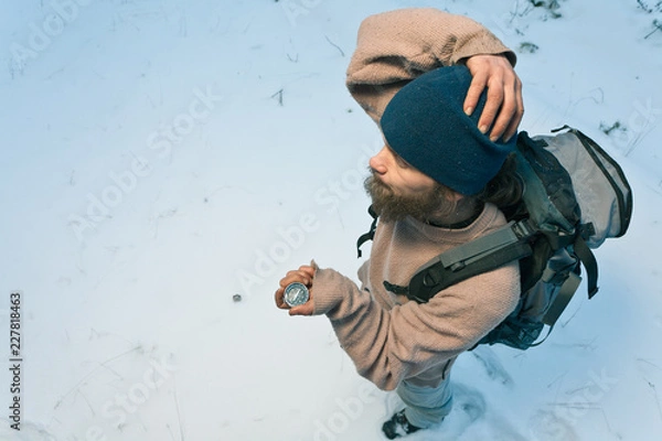 Fototapeta bearded confused traveller with compass in winter forest tries to find his way, top view