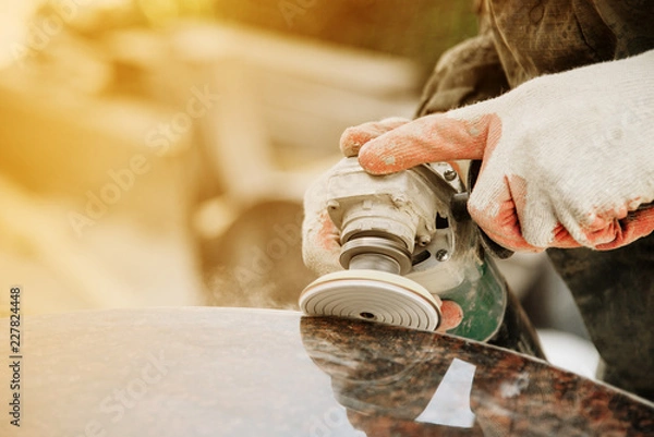 Obraz close-up a man in gloves polishes a marble monument with an angle grinder on a blurred background. grinding stone.