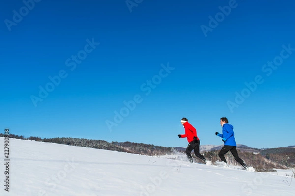 Fototapeta A side view of senior couple jogging in snowy winter nature. Copy space.