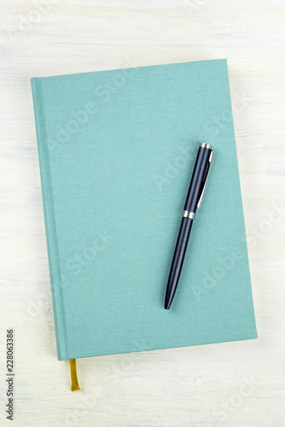 Fototapeta A photo of a teal blue journal with a pen, an elegant notebook or planner with copy space, shot from the top