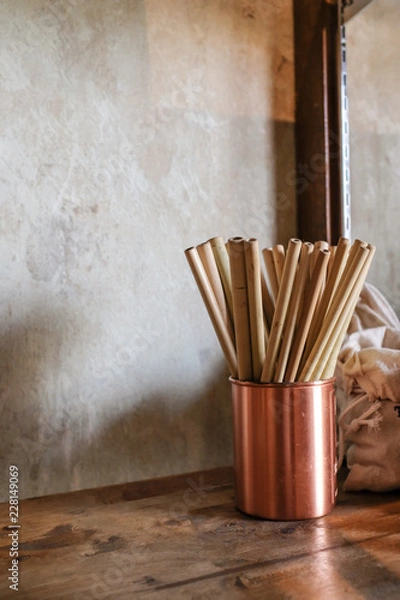 Obraz Vertical photo of natural color bamboo straws in rose gold bronze cup  on wooden table with loft concrete background