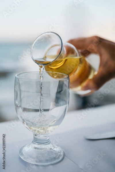 Obraz A woman's hand with a bottle of white wine pouring wine into a glass