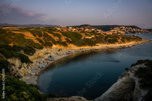 Fototapeta Beach of limestone rock S`Archittu di Santa Caterina, Oristano Province, Sardinia, Italy captured at beautiful sunset with lot of unrecognizable people on the beach.