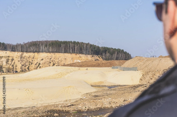 Fototapeta A man looks at the sand pit and the forest in the background.