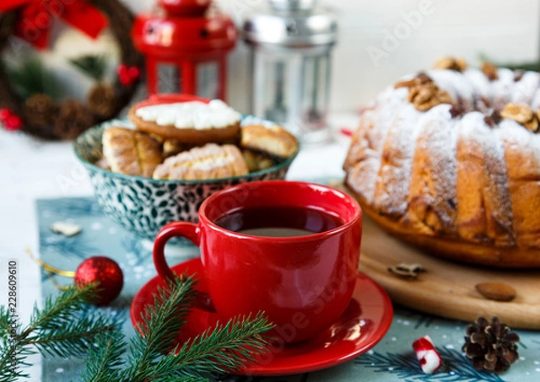 Fototapeta Fruitcake, decor, branches of spruce, plate with a cake and red cup of coffee or tea on the gray wooden table. New year and Christmas decoration concept.  copy space
