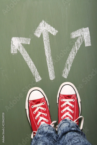 Fototapeta Young person standing in front of three arrows showing different ways