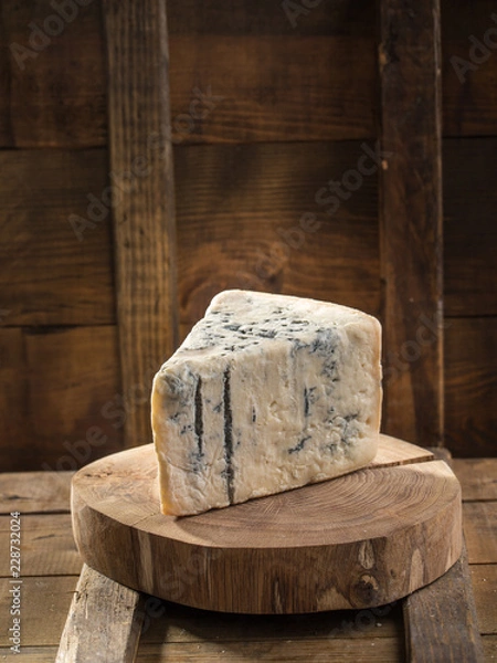 Fototapeta Slice of blue cheese on wooden board on dark background