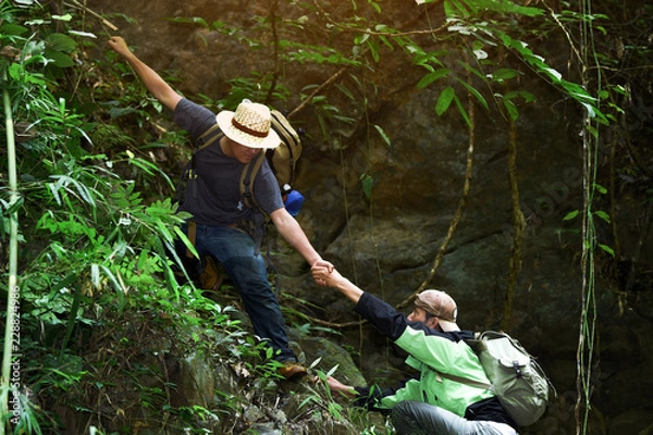 Fototapeta Help and assistance concept.Two male hikers climbing up mountain cliff and one of them giving helping hand.
