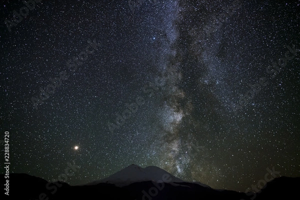 Obraz Stars of the Milky Way at night in the sky above Mount Elbrus. View of the northern slope of the two peaks of the stratovolcano. The highest peak of Russia and Europe is 5642m. 
