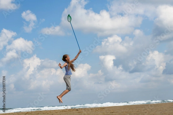 Fototapeta girl in a  in striped t-shirt on the sea catches clouds by a net on a sunny day