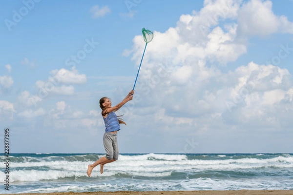 Fototapeta girl in a  in striped t-shirt on the sea catches clouds by a net on a sunny day