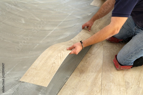 Fototapeta Work on laying flooring. Worker installing new vinyl tile floor.