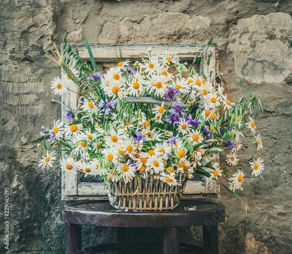 Fototapeta Bouquet of wild camomile and cornflowers with a rustic window and an old wall in the background.