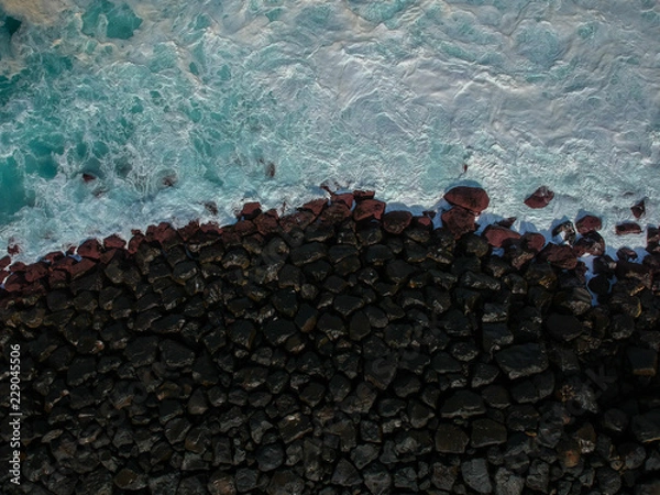 Fototapeta Aerial top view of sea waves hitting a stones from a jetty in pier. Drone view