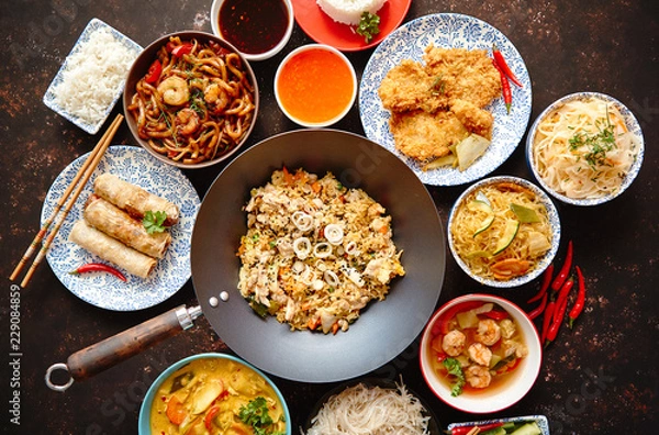 Fototapeta Asian food set. Noodles, fried rice with chicken, tom yum soup, spring rolls, deep fried fish and udon with prawns. Top view on dark rustic background. Oriental style food concept composition.