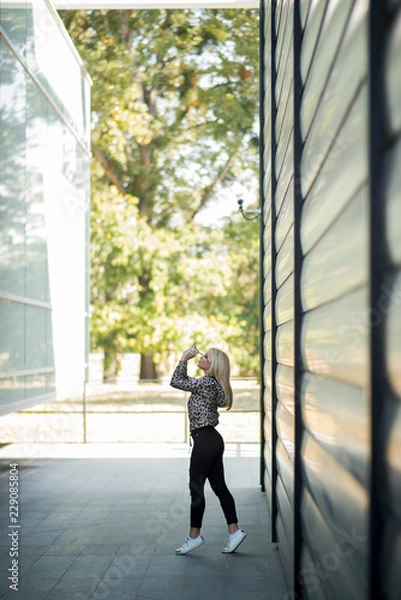 Fototapeta Photographing a girl during autumn near a high-tech glass building with a blurred background of the park