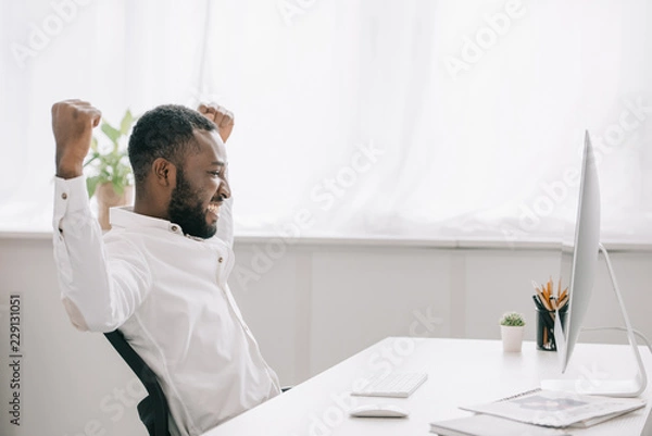 Obraz side view of happy african american businessman working at computer in office and showing yes gesture