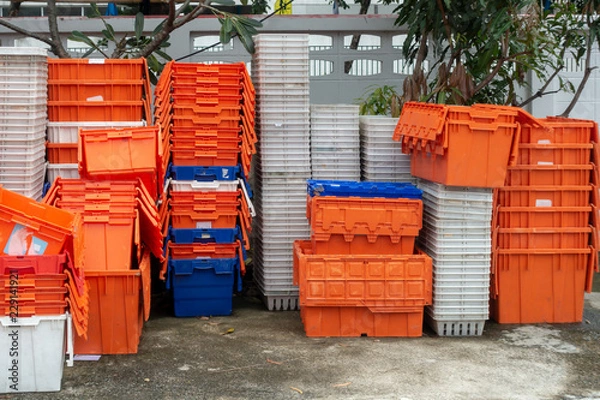 Fototapeta Ułożone stary plastikowy kosz i pudełka w kolorze pomarańczowym, niebieskim i białym na betonowej podłodze z drzewem i betonowym ogrodzeniem w tle