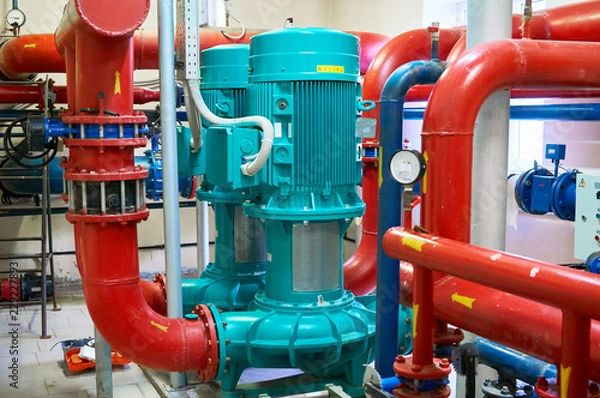 Obraz Two vertical engines painted blue with pumps connected to pipes painted red.