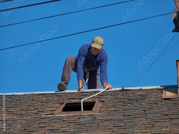 Fototapeta Maintenance of the roof of an old village house with slate tiles.