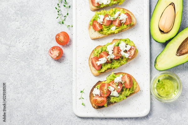 Fototapeta Avocado cherry tomatoes feta cheese toasts on board. Top view, space for text.