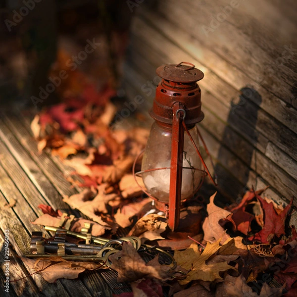 Fototapeta Old oil lantern burning at retro wooden bench with dry fallen leaves. Autumn concept image. 