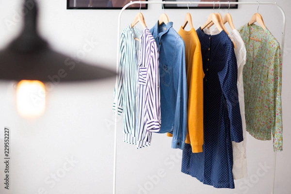 Fototapeta Clothes hang on wooden coat hangers in clothing store with home tone. Shopping and spending concept